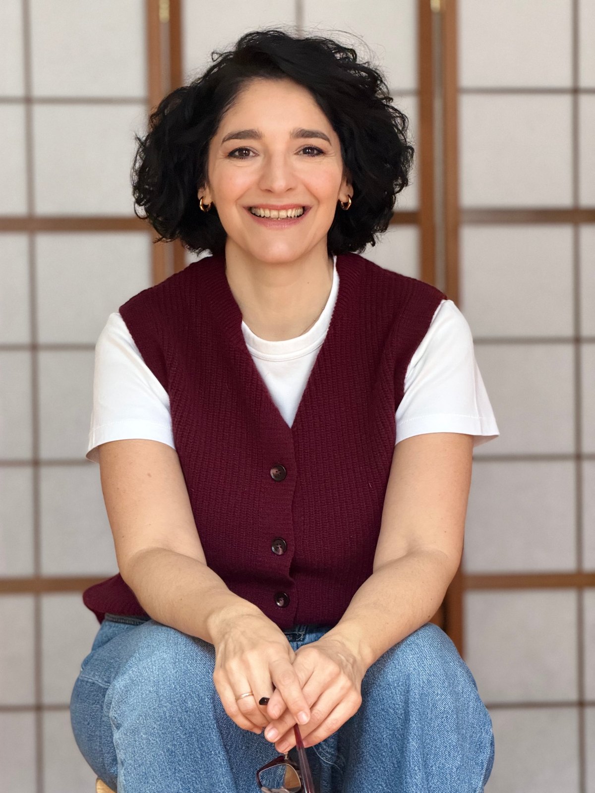 Portrait of Irini smiling, seated in front of a paper screen